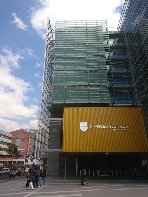 A building of the Universidad Catolica de Colombia with a glass façade can be seen with a building with an exposed brick façade in the background